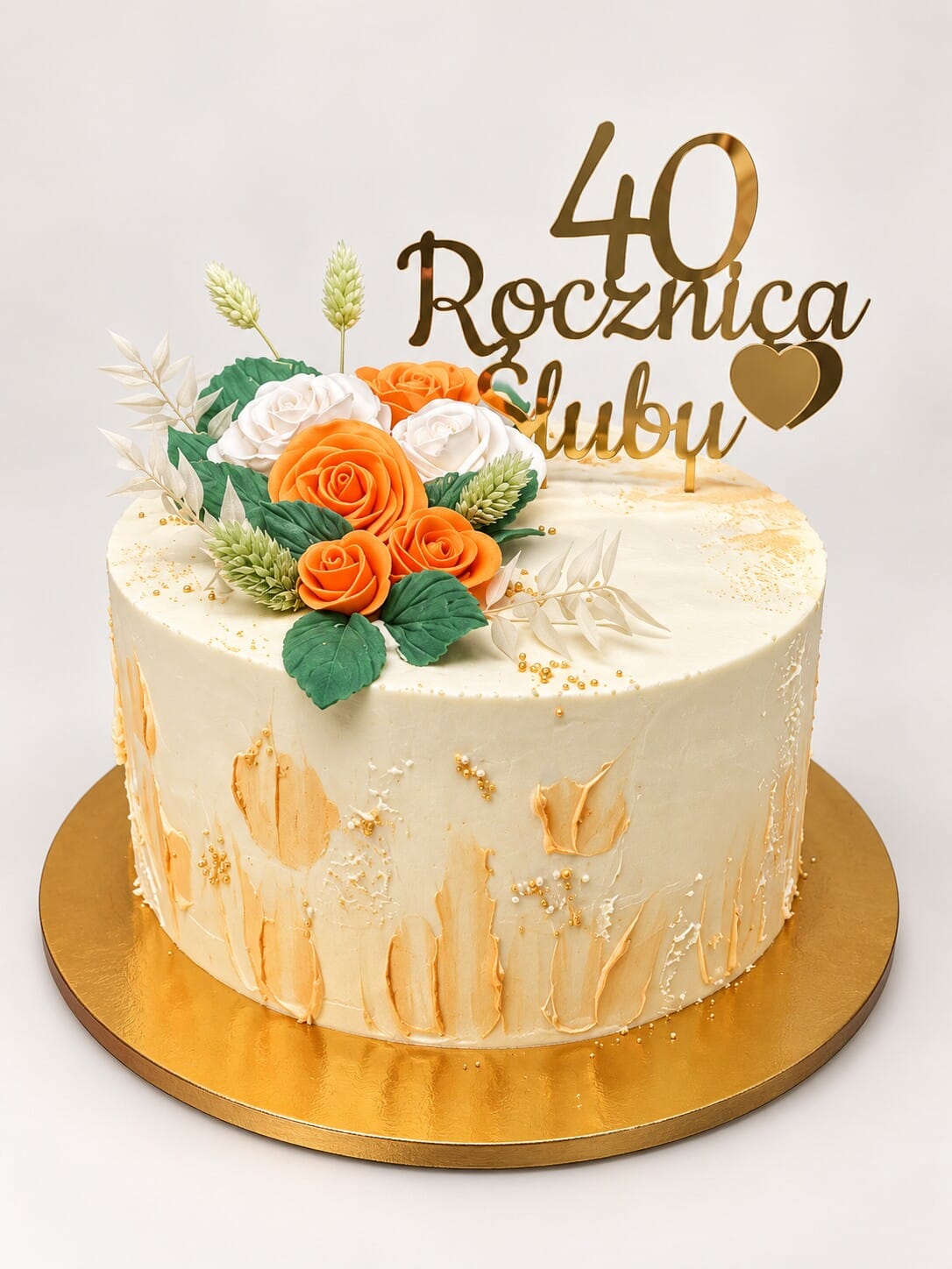 Kremowy tort z pomarańczowymi i białymi różami, zielonymi liśćmi, złotymi akcentami i topperem „40 Rocznica Ślubu” na złotym podkładzie.